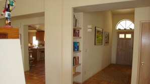 Un pasillo con suelo de baldosas, una estantería y una puerta que da a otra habitación.