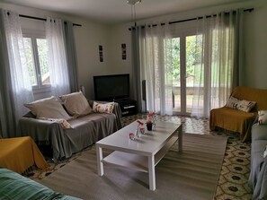 A living room with a sofa, a coffee table, and a television. There are curtains on the windows, and a rug on the floor. - LARGE VILLA 12 PERS. 5 mn from the beaches. LARGE SWIMMING POOL AND 2000m2 LAND. (Six-Fours-Les-Plages)