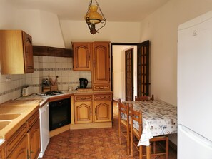 A compact kitchen with wooden cabinets, a gas stove, a sink, and a dining area with a table and chairs.