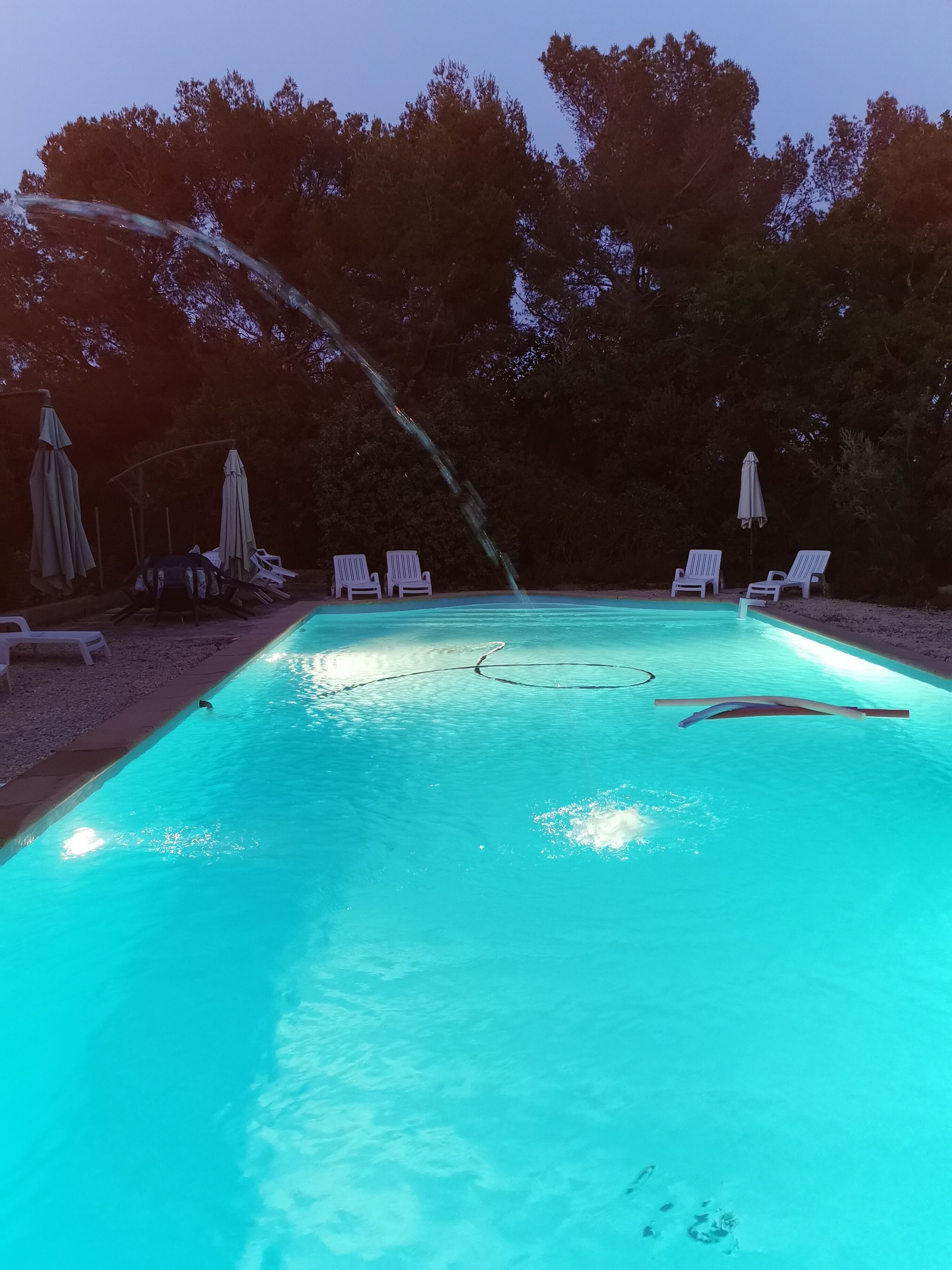 A swimming pool with a water feature, surrounded by lounge chairs and umbrellas.