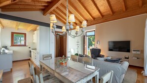 Une cuisine moderne avec des meubles en bois, une table à manger avec des chaises, un lustre et un coin salon avec un canapé et un téléviseur.