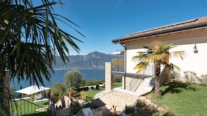 Une terrasse offrant une vue sur un lac et des montagnes, avec des murs en pierre et un palmier.