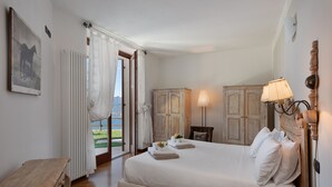 Une chambre spacieuse avec un grand lit, un banc en bois et une vue sur l’extérieur grâce à une porte ouverte.