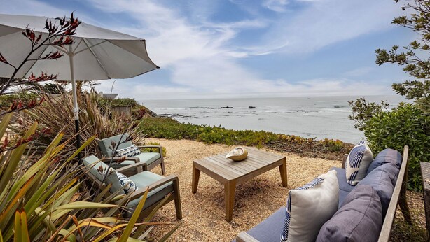 A coastal outdoor seating area with a table, chairs, and an umbrella, overlooking the sea.