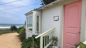 A coastal house with a pink door, a small porch, and a view of the ocean.