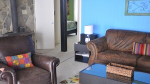 A living room with a stone wall, a fireplace, a brown leather sofa, a colorful pillow, a small table, and a blue wall. - Close proximity to Hawksnest, Otter Falls -- and all the High Country offers! (Seven Devils)