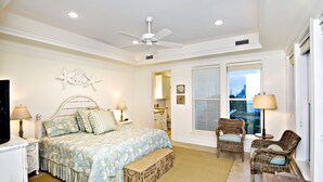Ein Schlafzimmer mit einem Bett, zwei Stühlen, einem Deckenventilator und einem Fenster mit Jalousien.