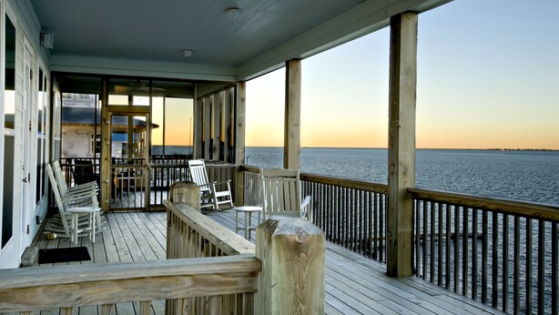 Eine Holzterrasse mit Stühlen und Blick auf das Wasser bei Sonnenuntergang.