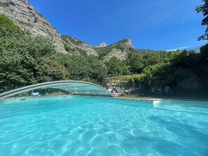 Une piscine à l’eau claire, entourée de verdure et avec une chaîne de montagnes en toile de fond.