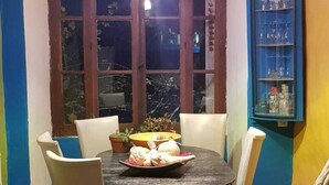 A dining area with a round table, four chairs, a window with curtains, a shelf with glasses, and a colorful tiled floor. - Into the wild: Charming house, surrounded by nature, large private pool. (Romeyer)