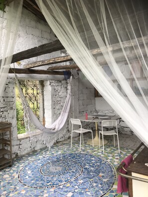 A rustic room with a hammock, a round table with chairs, and a patterned floor. - Into the wild: Charming house, surrounded by nature, large private pool. (Romeyer)