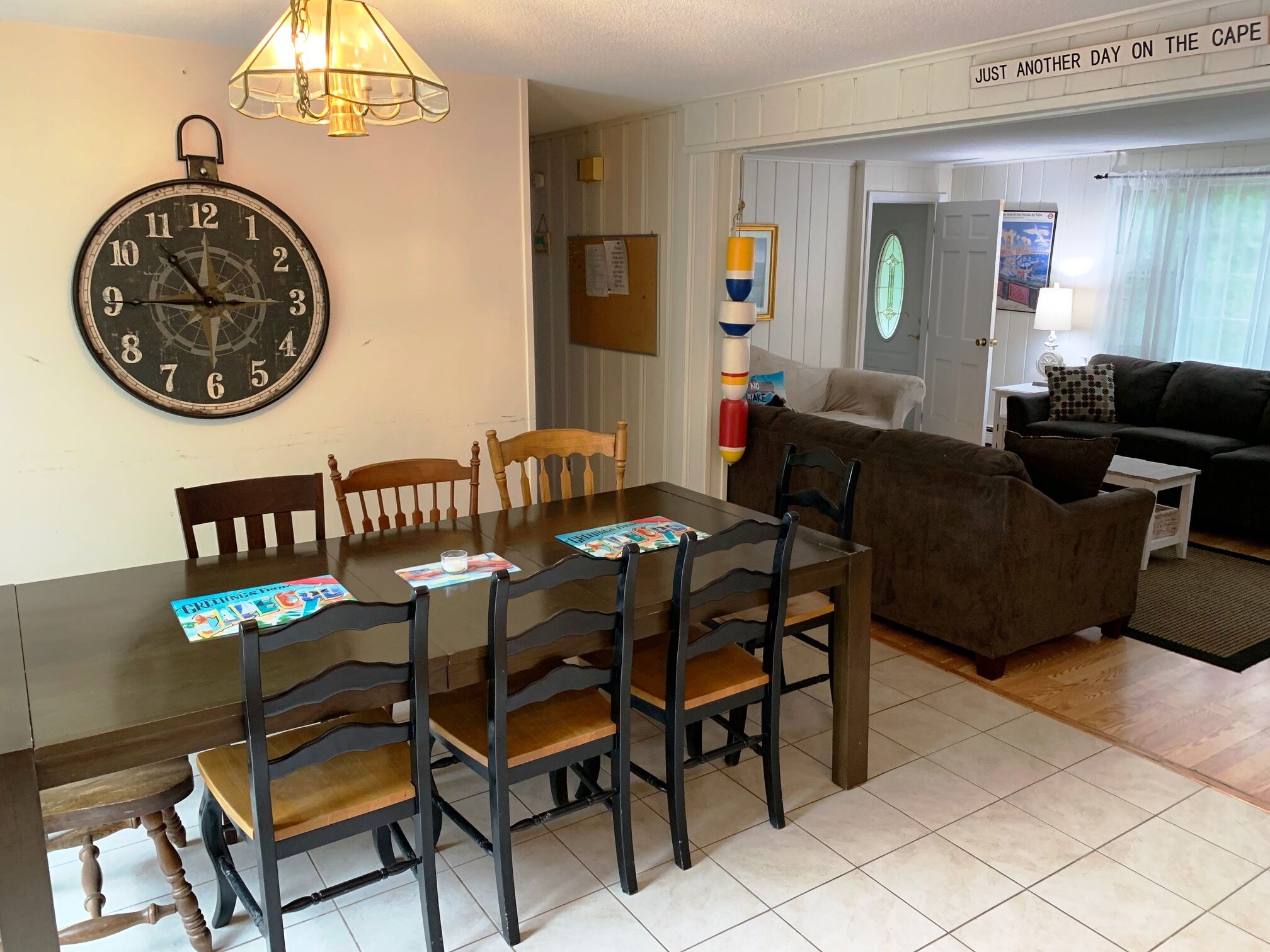 Un coin repas avec une table et des chaises en bois, une horloge murale et un canapé à l’arrière-plan.