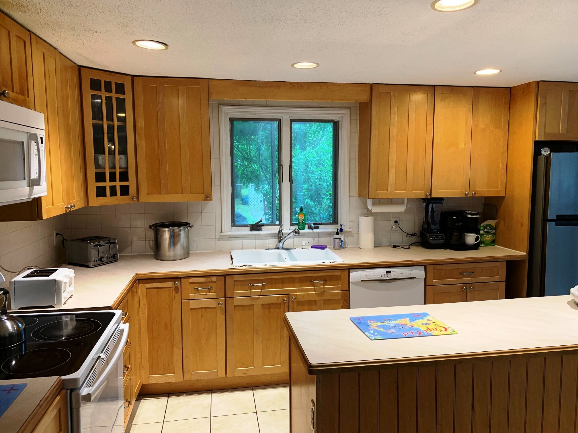A kitchen with wooden cabinets, a microwave, a toaster, a sink, and a window with a view of greenery.