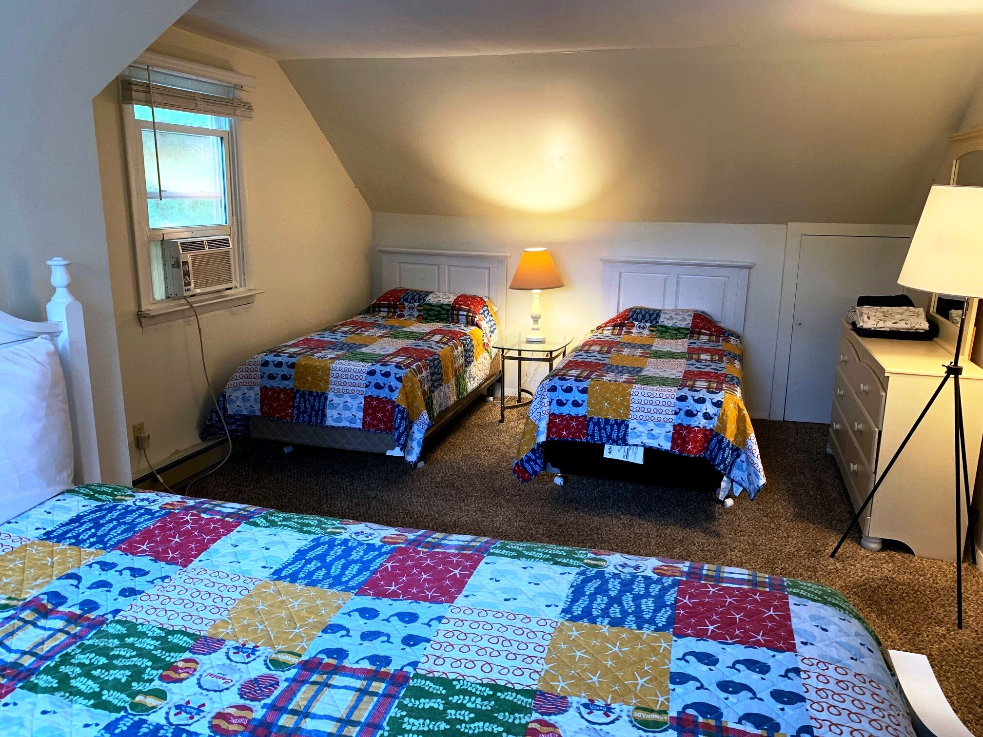 Un dormitorio con dos camas, una ventana con persianas, una lámpara y un aparador.