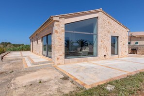 A modern stone building with large glass windows, a patio area, and a view of palm trees. - modern converted farmhouse with pool, quiet location (Santanyí)
