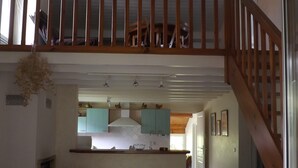 Un vaste espace de vie doté d’un haut plafond, d’un escalier en bois, d’une cuisine avec des meubles de couleur turquoise et d’un coin repas agrémenté d’une table en verre.