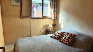 Ein Schlafzimmer mit einem Bett, einem Nachttisch, einer Lampe und einem Fenster mit Vorhängen.