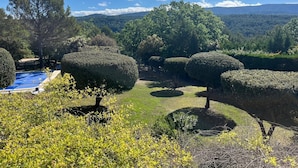 Un jardín ajardinado con tupers cuidadosamente podados, una piscina y vistas a colinas distantes.