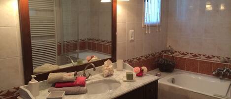 A bathroom with a large mirror, two sinks, a bathtub, and decorative items on the counter.