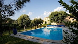 Una piscina rodeada de césped cuidado y árboles, con un edificio al fondo.