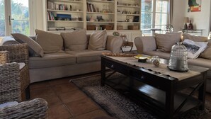 Una sala de estar acogedora con un sofá color beige, una mesa de centro de madera y una amplia estantería blanca llena de libros y objetos decorativos.