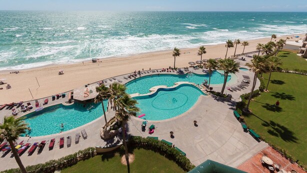 A resort with a large pool, beach access, and palm trees.