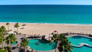 A resort with a large swimming pool, palm trees, and a beach.