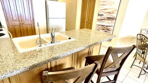A kitchen with granite countertops, a double sink, wooden cabinets, and two bar stools.