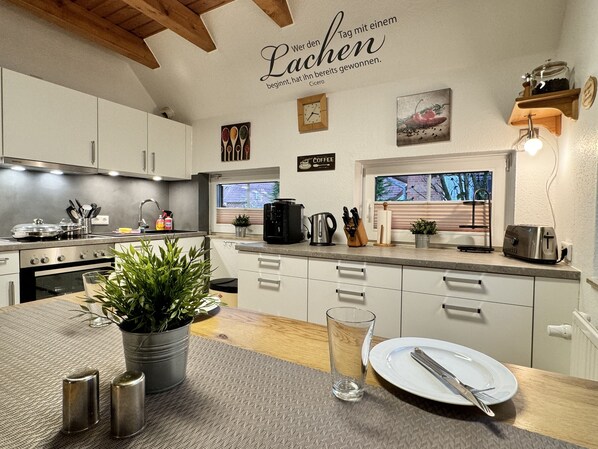 A modern kitchen with white cabinets, stainless steel appliances, and a wooden ceiling.