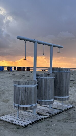 A beach scene with wooden barrels and metal structures, possibly for water activities, under a cloudy sky.