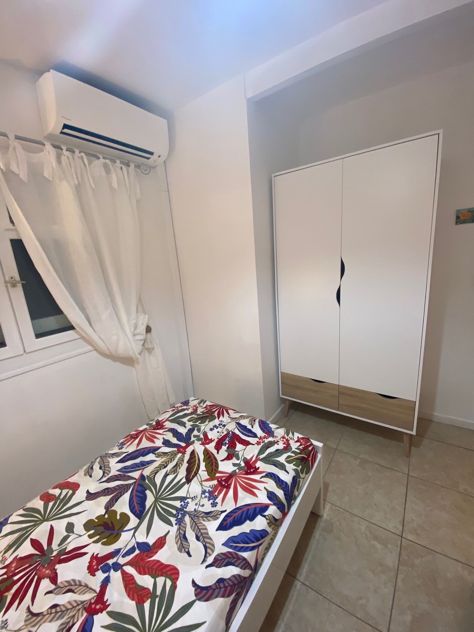 Un dormitori amb un llit, un armari i una finestra amb cortines.