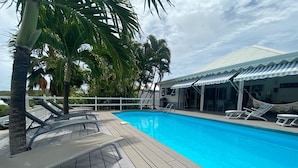 En pool med træterrasse, palmer og et overdækket siddeområde.