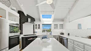 Uma cozinha moderna com uma ilha central, armários brancos, fogão preto e um claraboia.