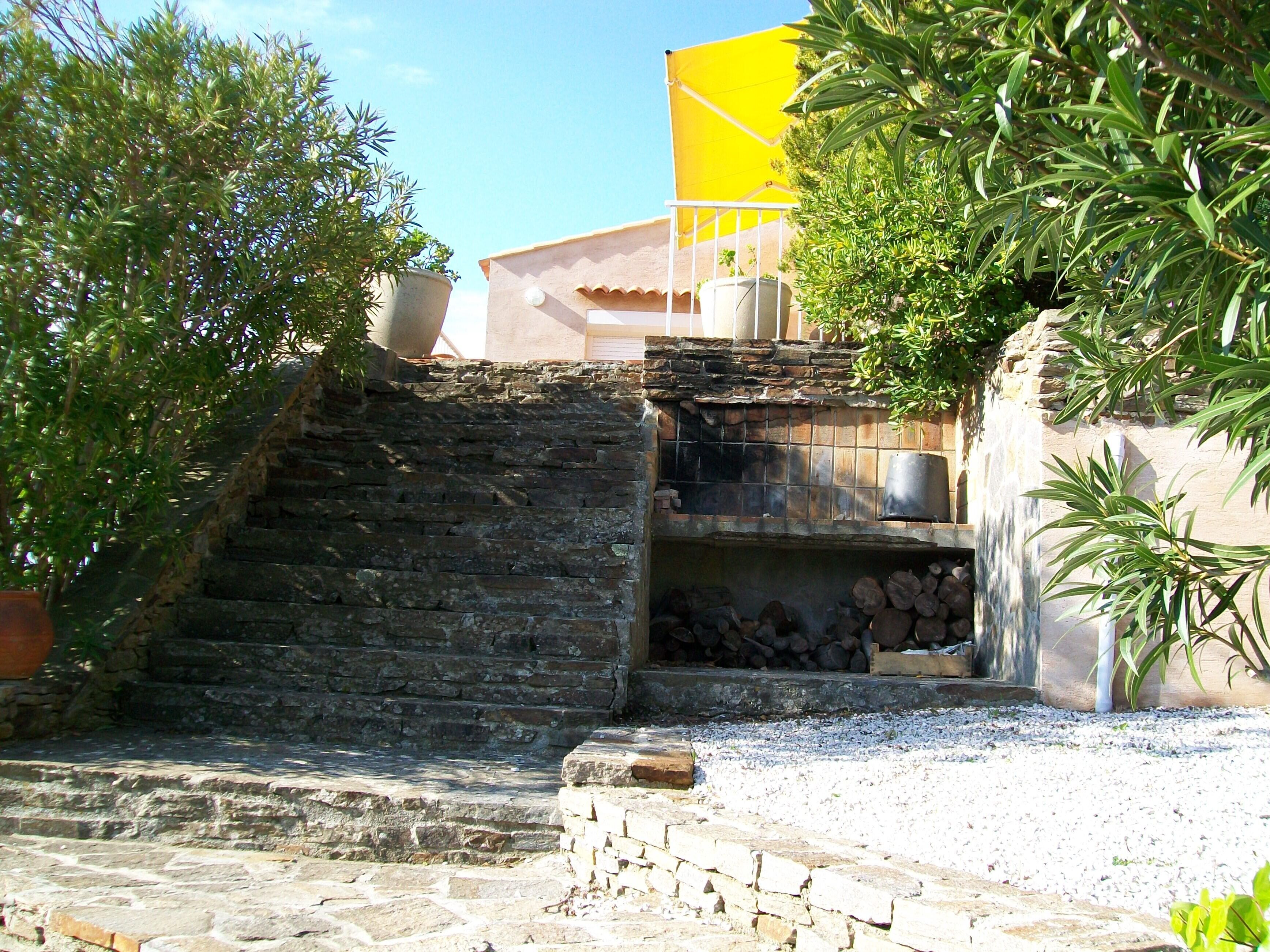 Un escalier en pierre mène à un mur de pierre sur lequel se trouve une petite étagère en bois et une fontaine.