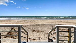 A beach with a wooden walkway leading to the water, a pile of driftwood, and a clear blue sky. - Comfortable Beach House on the Sand (Aptos)