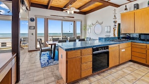 A kitchen with wooden cabinets, a blue countertop, and a view to the ocean. - Comfortable Beach House on the Sand (Aptos)