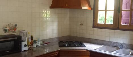 A kitchen with white tiled walls, a stove, an oven, a microwave, and wooden cabinets.