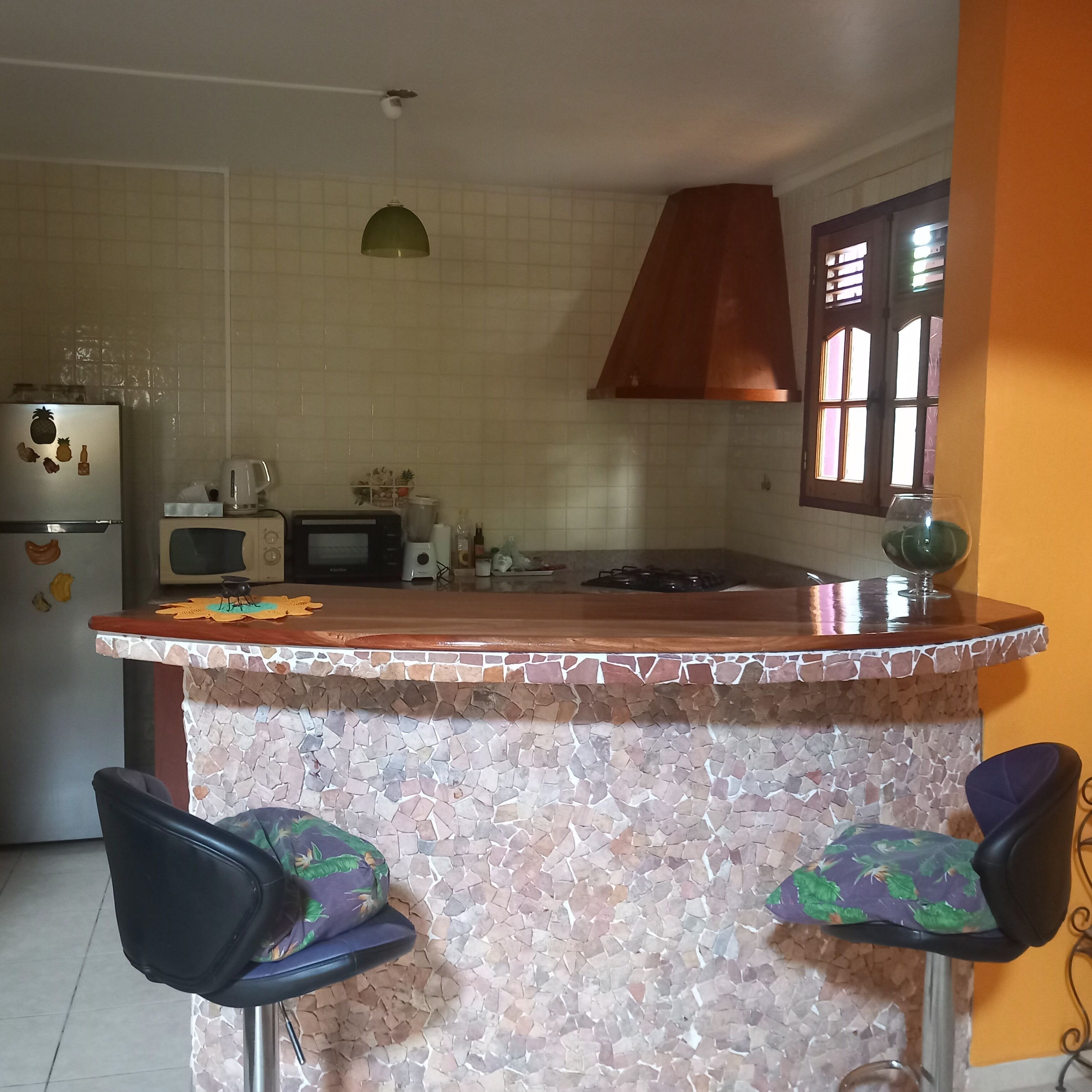 A kitchen with a stone countertop, a microwave, a refrigerator, and two chairs with patterned cushions.