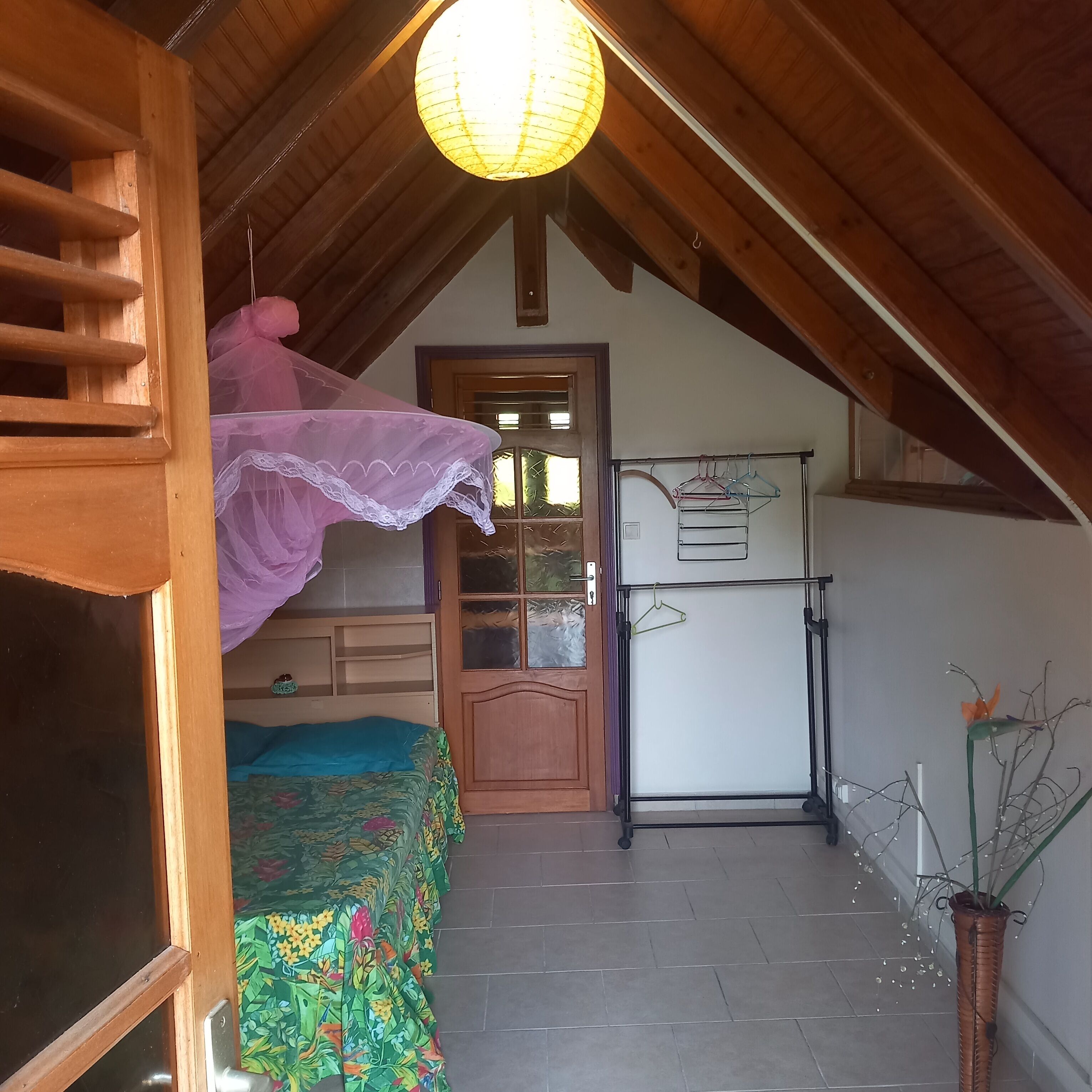 A bedroom with a bunk bed, a small desk, a wardrobe, and a hanging clothes rack.