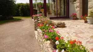 Un chemin de pierre mène à une véranda dotée d’une porte en verre, qui est elle-même entourée de plantes et de fleurs en pot.