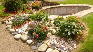 Un jardin où l’on trouve une grande variété de plantes et un élément décoratif aquatique en pierre.