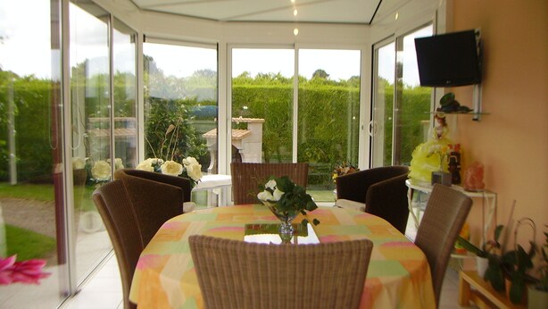 Une véranda avec une table et des chaises, un vase rempli de fleurs et un téléviseur accroché au mur.