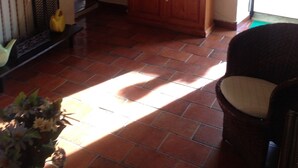 Una sala de estar con un televisor sobre un mueble de madera, un sofá y una puerta que da al exterior.