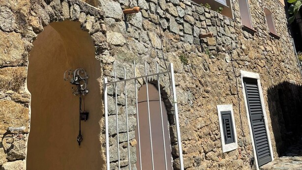 Un edificio de piedra con una verja metálica, un ventanal pequeño y un balcón con toldo blanco.