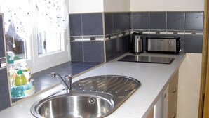 A modern kitchen with a stainless steel sink, two toasters, and a window with decorative curtains.