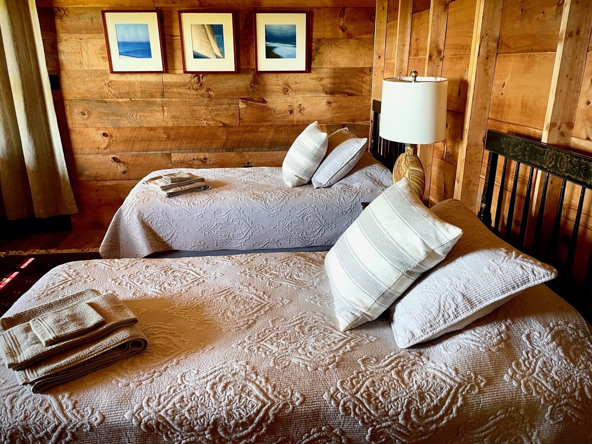 Ein gemütliches Zimmer mit zwei Betten, einer Lampe und gerahmten Bildern an der Wand.