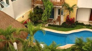 Une piscine entourée d’une végétation luxuriante et bordée d’une structure à toit de chaume.