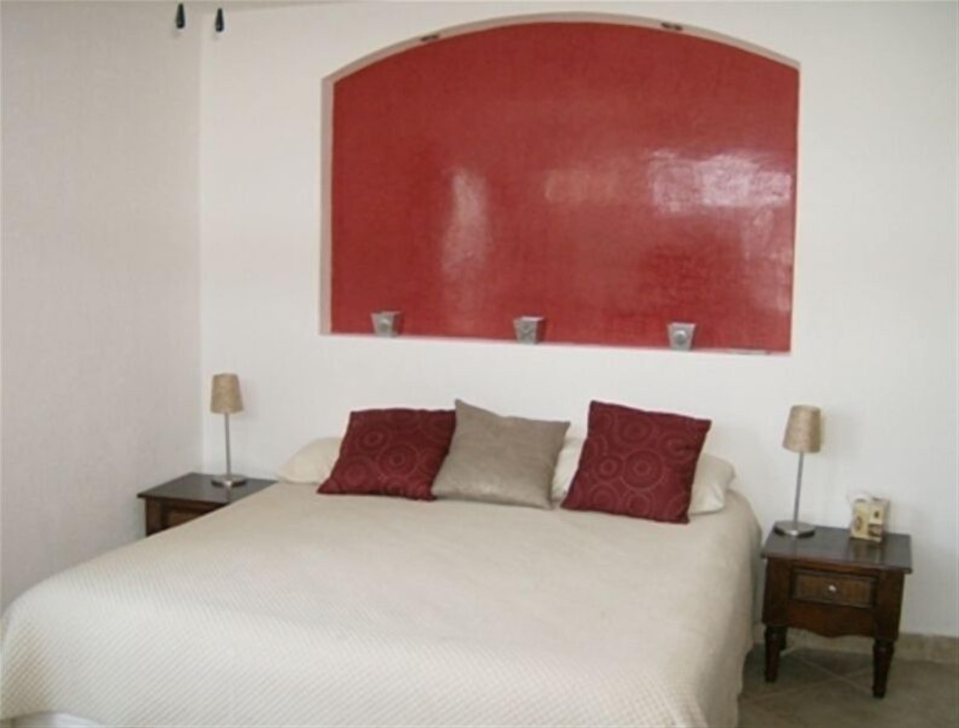 A bedroom with a large bed, two bedside tables, and a red accent wall.
