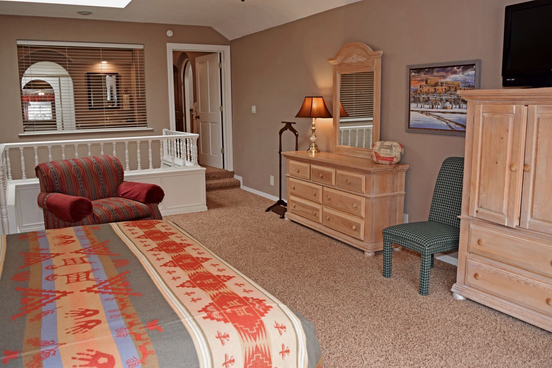 A bedroom with a bed, a dresser, a chair, a lamp, a window with blinds, and a painting on the wall.