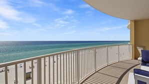 En balkon med udsigt over havet, en sandstrand og et par personer.